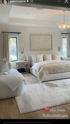 a large white bed sitting inside of a bedroom next to two windows and a chandelier