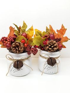 two mason jars filled with pine cones, berries and other autumn decorations sitting on top of a table