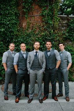 a group of men standing next to each other in front of a green plant covered wall