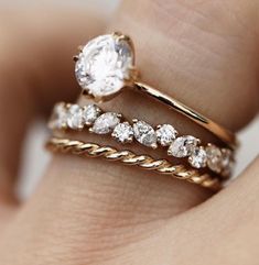 a woman's hand holding two rings with diamonds on them and the ring is gold