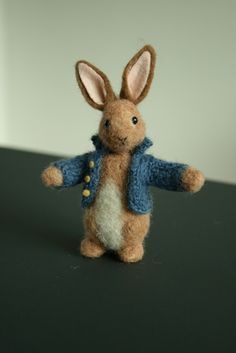 a small stuffed rabbit wearing a blue jacket and standing on it's hind legs