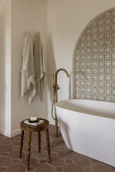 a white bath tub sitting in a bathroom next to a wooden stool and wall mounted towel rack