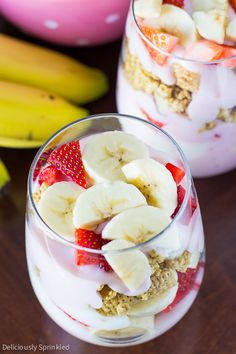 two glasses filled with yogurt, strawberries and banana's on a table