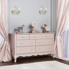 a white dresser sitting next to a window covered in pink curtains