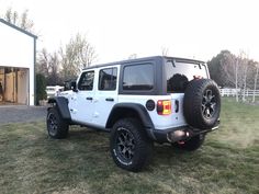 a white jeep parked on top of a grass covered field next to a garage door