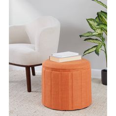 an orange ottoman sits next to a white chair and potted plant on the floor