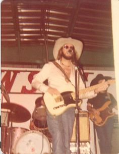 a man in a cowboy hat playing guitar and singing into a microphone while standing next to another man