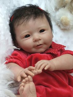 a baby doll that is laying down on a white blanket with feathers around it's head