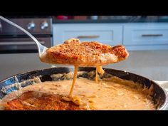 a pizza being lifted from a skillet by a spatula with gravy