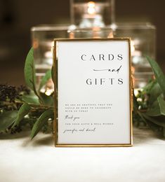 a card and gift box sitting on top of a table with greenery next to it