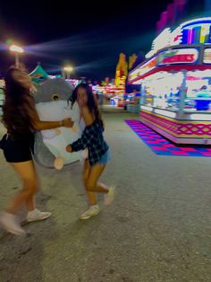 two girls are playing with a stuffed animal in front of a carnival ride at night