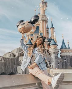 a woman sitting on top of a stone wall next to a castle with lots of balloons