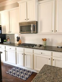 a kitchen with white cabinets and granite counter tops, stainless steel microwave above the stove