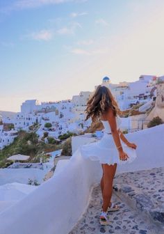 a woman in a white dress is walking up some steps with her hair blowing in the wind