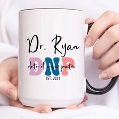 a person holding a white coffee mug with the words dr ryan on it in pink and blue