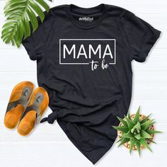 a black t - shirt with the words mama to be on it next to some shoes