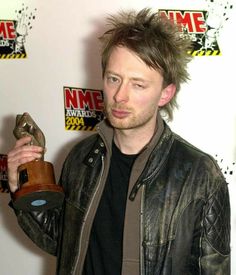 a man holding an award in his right hand and wearing a leather jacket on the other