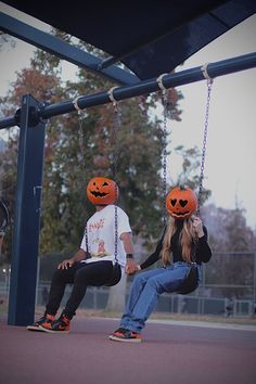 two children sitting on swings wearing pumpkin heads