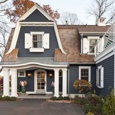 a blue house with white trim and shutters on the front door is surrounded by fall foliage