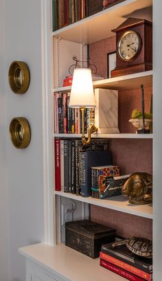 a book shelf with books and a lamp on it next to a wall mounted clock