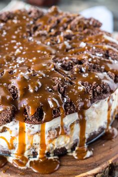 a cake covered in ice cream and caramel drizzle on top of a wooden plate