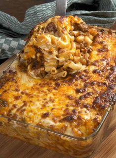 a casserole dish with noodles and meat in it on a wooden table next to a fork