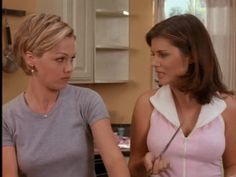 two women standing in a kitchen preparing food on a cutting board and one is holding a knife