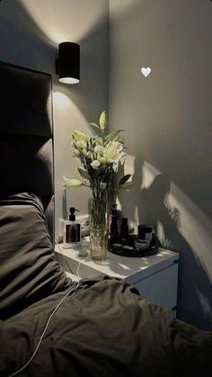 a vase with flowers sitting on top of a bed next to a night stand and lamp