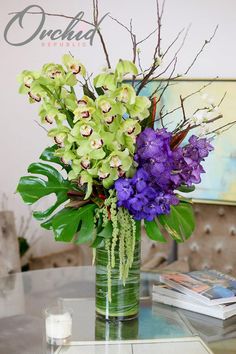 a vase filled with purple and green flowers on top of a glass table next to a couch