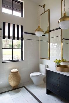 a white bathroom with black and gold accessories on the vanity, toilet and window in the background