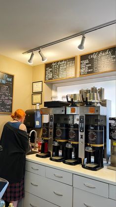 a woman standing in front of a counter filled with lots of coffee machines and cups