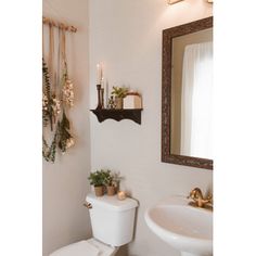 a white toilet sitting next to a sink under a bathroom mirror with candles on it