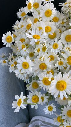 white and yellow flowers are in the middle of a blue vase on top of a chair