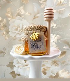 a jar of honey sitting on top of a white cake plate next to a wooden stick