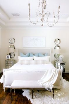 a white bed sitting in a bedroom on top of a hard wood floor next to a chandelier