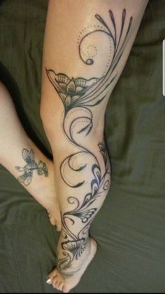 a woman's legs with tattoos on them sitting on top of a green bed