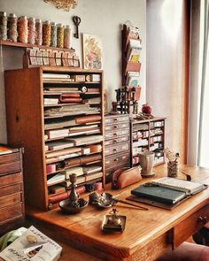 a wooden desk topped with lots of books next to a dresser filled with papers and knick - knacks