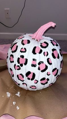 a white and pink painted pumpkin sitting on top of a brown cloth covered tablecloth