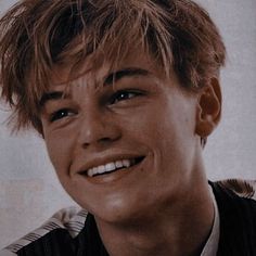 a close up of a person wearing a vest and smiling at the camera with his hair pulled back