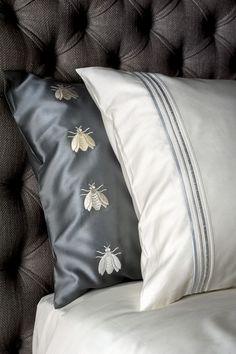 a bed with two black and white pillows on it's headboard, one has a bee embroidered on the pillow