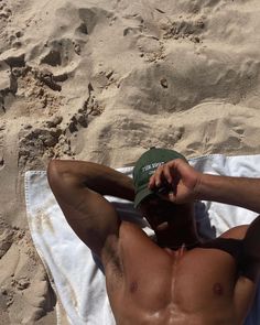 a shirtless man laying on top of a beach next to a white and blue towel