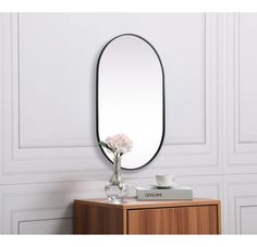 an oval shaped mirror sitting on top of a wooden table next to a vase with flowers