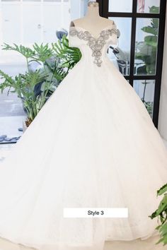 a white wedding dress on display in front of a window with potted plants behind it