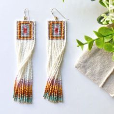 two pairs of beaded earrings sitting on top of a table next to a potted plant