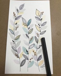 a drawing of leaves and berries on white paper next to a black ink pen,