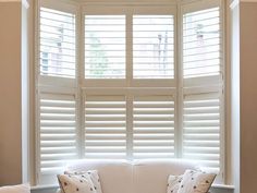 a white couch sitting in front of a window with shutters on both sides and pillows on the back