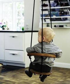 a baby sitting on a swing in a kitchen