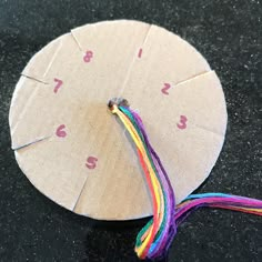 a clock made out of paper with colorful thread on the side and numbers painted on it