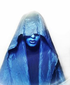 a woman with blue makeup and a hooded cloak over her head is looking at the camera