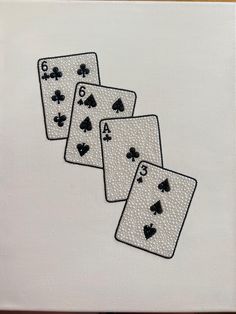 four playing cards are embroidered onto the back of a white canvas with black stitching